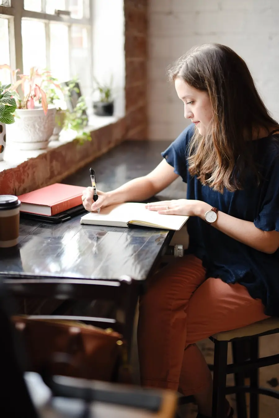A woman writing in a journal at a table by a bright window